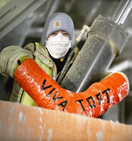 A masked Stop Cop City protester locked down to Brasfield & Gorrie construction equipment in Midtown Atlanta in March 2024. The orange lockbox they are employing reads "Viva Tort" in memory of Tortuigata.