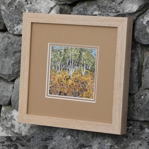 Same framed artwork sitting against a stone wall, viewed on an angle from the right.