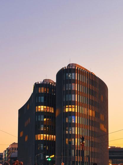 Photo of a modern office or commercial building during the golden hour. Some windows are illuminated.