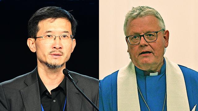 Links: Ein Mann mittleren Alters mit schwarzen Haaren, Oberlippen- und Kinnbart, konzentrierter Blick, dunkles Jackett und schwarzes Hemd, spricht in ein Mikrofon. Rechts ein Mann mit grauem Haar, blauem Bischofsgewand und weißer Stola.