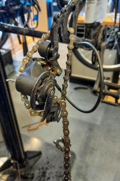 Gros plan sur la partie arrière d'un vélo. La roue a été retirée. On voit le dérailleur fixé du mauvais côté, à l'intérieur du cadre, la chaîne passant dedans de façon anarchique.