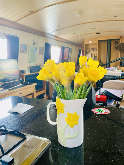 White jug with yellow daffodils painted on it. Fresh daffodils in the jug