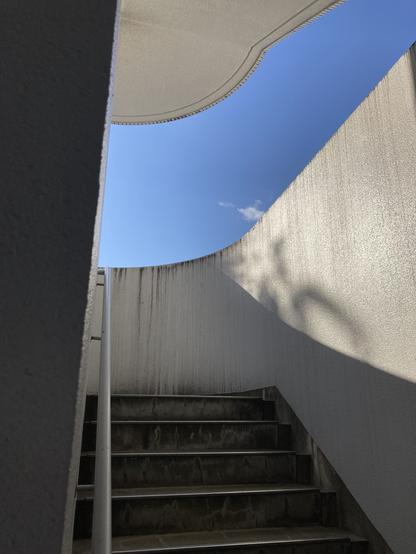 Looking up an open-air staircase, and bright blue sky with a tiny cloud floating in it, behind the staircase.