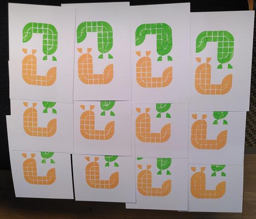 Postcard sized lego prints spread to dry. They show a green slug and an orange slug. They are leaning towards each other forming a loose circle shape, looking a bit like the ying yang symbol.
