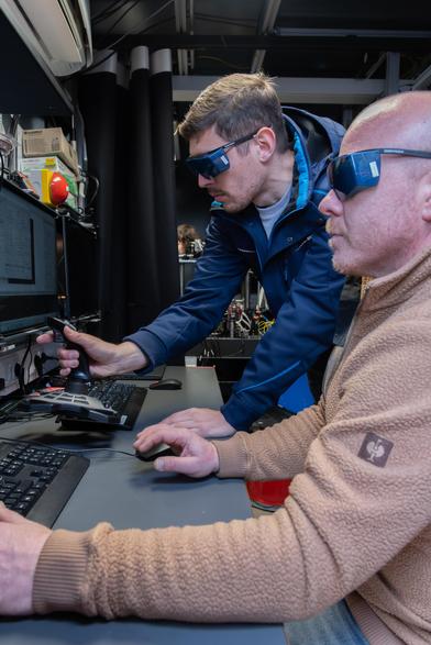 Two scientists wearing laser safety glasses and working inside the ground station.
