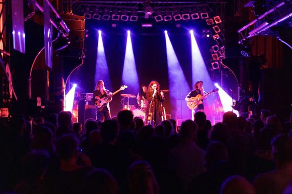 Szene aus einem Konzert im Hamburger Knust: Der Konzertsaal ist voll, Blick von hinten über das Publikum auf die lila illuminierte Bühne.