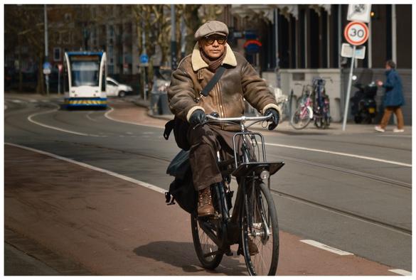 A person riding a bicycle. He is wearing a leather jacket reminiscent of an old aviator.