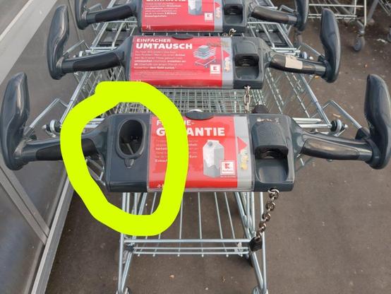 Foto einer Reihe Einkaufswagen. Der erste hat ein 2-3 Finger breites senkrechtes Loch in der Plastikflache zwischen den Griffen, das nach unten etwas schmaler wird