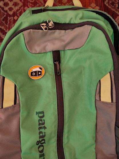 Ein Button mit dem Logo der Computertruhe, auf einem grünen Rucksack.