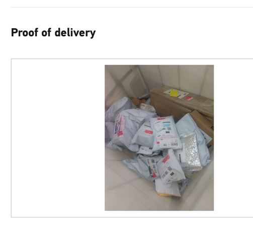 Screenshot says Proof of delivery' photo is of a pile of identical white parcels and a cardboard box in a tiled area