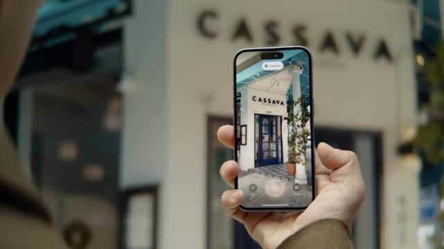 Ein iPhone mit geöffneter Kamera wird auf ein Haus gehalten, das den Namen „Cassava“ trägt und offenbar ein Geschäft oder Restaurant ist.