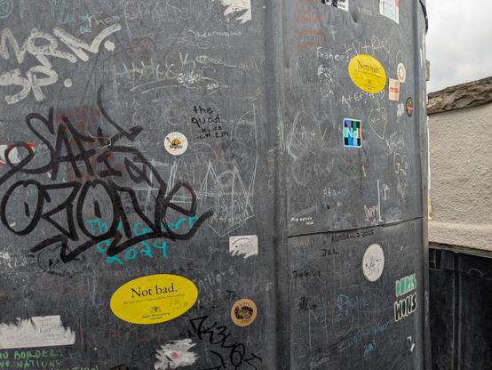 Two "nett hier" stickers (one German, one English) on lead weatherproofing, amongst other stickers and graffiti