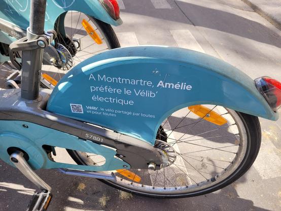 Roue arrière d'un velib électrique bleu sur lequel on lit "À Montmartre, Amélie préféré le Vélib électrique"