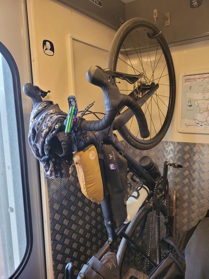 Vélo gravel noir suspendu à un anneau dans un train. Pins du logo Mastodon accroché à la sacoche de cadre