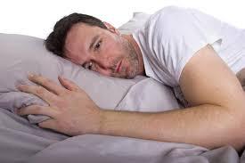 Image shows a man lying in bed looking depressed