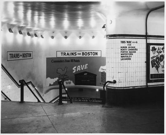 Black and white photo of an MTA station lobby, facing stairs leading down to a platform.  Wall signs read "TRAINS FOR BOSTON", "THIS WAY TO TRAINS FOR BOSTON - DORCHESTER - ASHMONT".  Stenciled on tiles on the right, labels direct readers to ~~the bus station~~ streetcars: "THIS WAY ➡️ for HURON AVENUE / NORTH CAMBRIDGE / PORTER SQUARE / WATERTOWN / WAVERLEY / LECHMERE".  Advertisements for Cambridge Savings Bank ("our 121st year!") and a rodeo show are also visible.