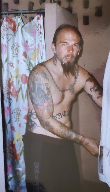 Heavily tattooed Shannon, with a long goatee, shaving, while inside a very basic guest house room in El Salvador.