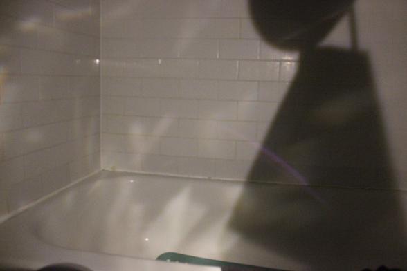 Mysterious reflection on walls of dark bathtub. Big shadow to the right.