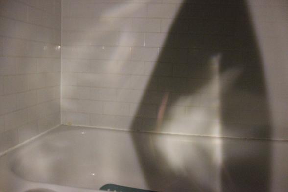 Mysterious reflection on walls of dark bathtub. Angular shadow to the right.