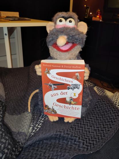 Stoffpuppe "Rattus Rattus" aus der CBBC-Serie "Horrible Histories" hält das Buch "Geschichten aus der Geschichte" des gleichnamigen Podcasts in den Pfoten