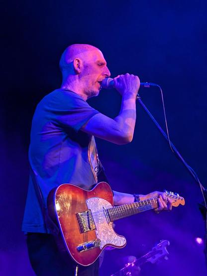 Bald man singing in to microphone while holding a red guitar