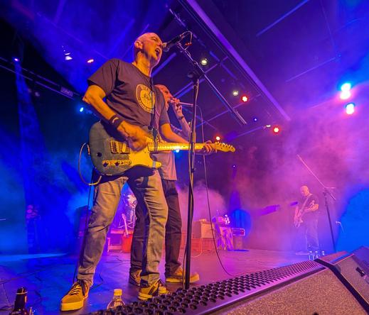 Guitarist and singer on stage. Bassist lurking in background under red and blue lights