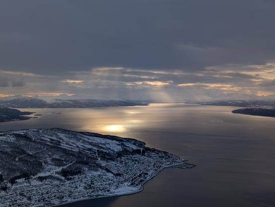 Looking from high up (666m) onto a fjord, sunrays light up spots on the water through grey clouds. Creating an almost lightning shaped pattern.