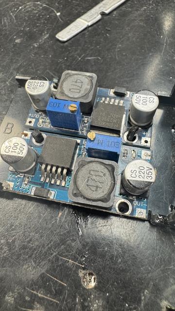 Two buck modules side by side with pieces of scrap ABS through their screw holes, being welded to the base below with acrylic cement (which works well for ABS too).