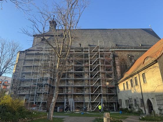 Großes Baugerüst an Südseite der Halleschen Moritzkirche. Die abendliche Frühlingssonne sendet ein paar Sonnenstrahlen und die Bauleute nehmen zum Feierabend ihre Helme ab.