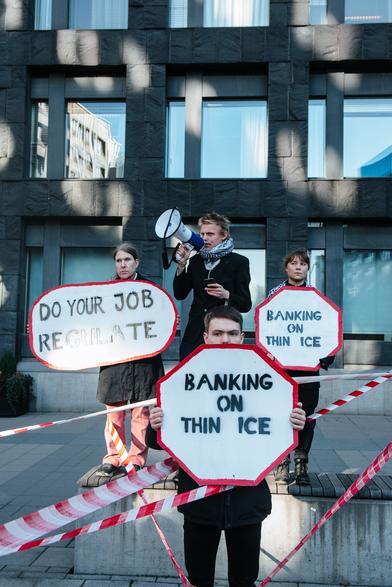 One person speaking on microphone and left we have one person with a placard saying "DO YOUR JOB REULATE", in right we have Greta with placard saying "Banking on think ice" and the same placard with the 4th person in front.