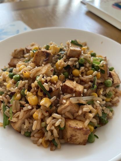 Rice, tofu and sweetcorn fried up together on a plate, with bits of green leek visible.