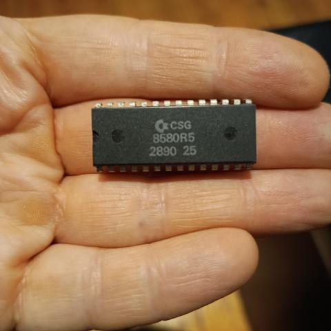 A SID chip from a C64C in my left hand. Model 8580R5, date code 2890.
