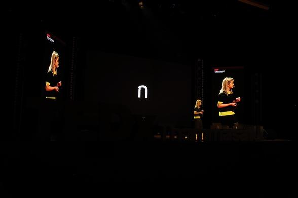 Boom speaking at TEDx ThammasatU, on the screen the Thai letter ก (Bilo Thai)