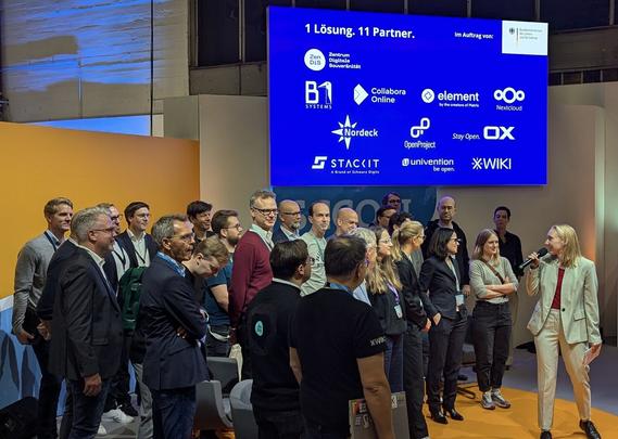 Me at the product launch of openDesk, talking in front of a group of people. Big screen in the background that says "1 Solution. 11 Partners."