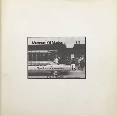 Un plan large de la devanture du musée, avec l’inscription au fronton : « Museum of Modern art ». On apperçoit Yoko Ono, situé en aplomb de l’espace entre les deux derniers mot tenant une pancarte avec la lettre « F ».