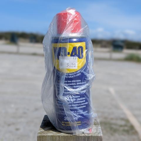 A bottle of WD40 in a plastic bag with a parking lot behind