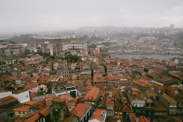 Bild von oben auf Porto bei schlechtem Wetter, grauer Himmel, Nebel am Horizont und Häuser mit roten Dächern sind zu sehen. Der Fluss Douro fließt durch die Stadt.