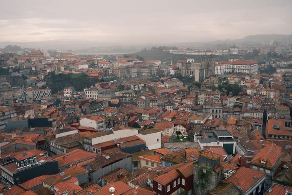 Bild von oben auf Porto bei schlechtem Wetter, grauer Himmel, Nebel am Horizont und Häuser mit roten Dächern sind zu sehen. Der Fluss Douro fließt durch die Stadt.