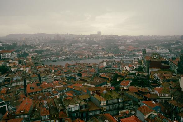 Bild von oben auf Porto bei schlechtem Wetter, grauer Himmel, Nebel am Horizont und Häuser mit roten Dächern sind zu sehen. Der Fluss Douro fließt durch die Stadt.