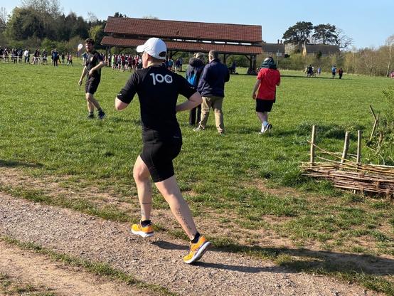 Photo of Emily running away from the camera. She is wearing her 100 Parkrun tshirt.