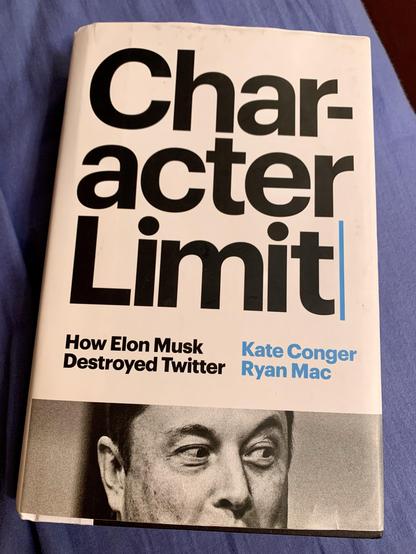 The image features the cover of a book titled "Character Limit: How Elon Musk Destroyed Twitter" by Kate Conger and Ryan Mac. The cover has a minimalist design with bold black text and a monochrome image of a person. The background is a blue linen.