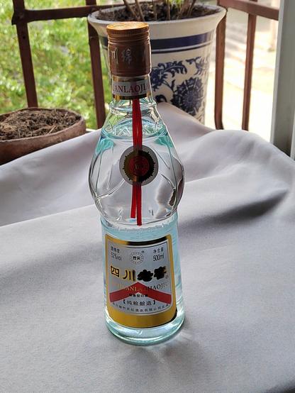 This is the bottle, pre-opening.  I've got it standing where I usually put out my tea presentations (because I had it set up already so why not?) backed by some potted plants and the sunny outdoors.

The bottle is fairly simple with only a little design flair.  The brand is noted—剑庄老窖 (Sword Estate Old Cellar)—along with the alcohol content (52%ABV) and volume (half a litre).  In addition it identifies the quality level as 纯粮酿造 (chún liáng niàng zào or "pure grain brew") indicating no additives are used beyond the traditional grain plus starter.

The liquid is purely transparent, like a bottle of water.

WATER OF DEATH!

OK, a bit over-dramatic, but still.  This is going to kick something fierce.