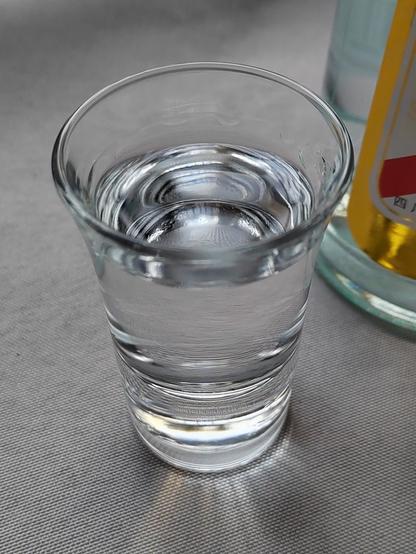 And here's a closeup of the shot.  The glass itself is a fairly standard double-sized shot glass.  It has a very thick bottom (to help keeping it upright) with a flaring rim.  The liquid fills about 3/4 of the glass, and even with the flaring rim and the short amount of time post-pour that this photo was taken some "angel's tears" or "legs" are starting to form.

The liquor itself is flawlessly transparent, with no visible impurities beyond a bubble or two left over from the pour.  It reflects ambient light nicely, and refracts it nicely as well.

Sitting there, it's filling the space (next to a wide open window!) with a floral sweet scent with interesting notes of pineapple and banana.  And anise?  Something sharp and spicy for certain.

Immediately after taking this photo I tossed back the shot and was pleasantly surprised at how smooth it was.  Given that this was only the three-year cellar process (in the enormous clay jars) this is astonishingly smooth.  I've had older liquors that were harsher than this.  The master distiller certainly knew what he was doing when brewing and distilling this hooch.

And at just a bit over 12RMB (US$2 at the time, though that won't last long now that the world has gone a bit dumber) this is an incredible find.