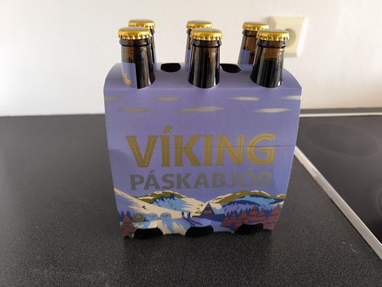 Un pack de 6 bouteilles de bière de la marque islandaise Viking. Les couleurs dominantes sont le mauve et le doré. L'illustration montre un scène hivernale avec une summer houses, un télésiège et des personnes qui pratiquent le ski.