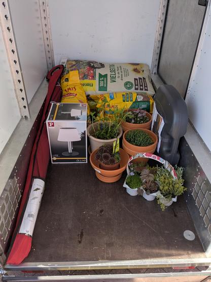 Blick in den Ladeflächen-Aufbau eines E-Lastenrads. Er ist beileibe nicht voll, obwohl viel drin ist. Die Ladung besteht aus Pflanzsubstraten, Tontöpfen, Pflanzen, einem Sonnenschirm und einer Outdoor-Solar-Tischlampe.
