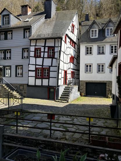 Ein total schiefes sehr schmales altes Fachwerkhaus in Monschau. Die Balken sind schwarz, die Gefächer weiß, Tür- und Fensterrahmen sind rot