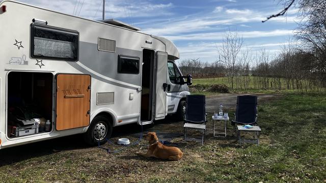 Unser Wohnmobil mit Ausblick über Wiesen. Neben dem WoMo stehen 2 Stühle, ein kleiner Tisch und Henry H.Lunke hat es sich gemütlich gemacht.