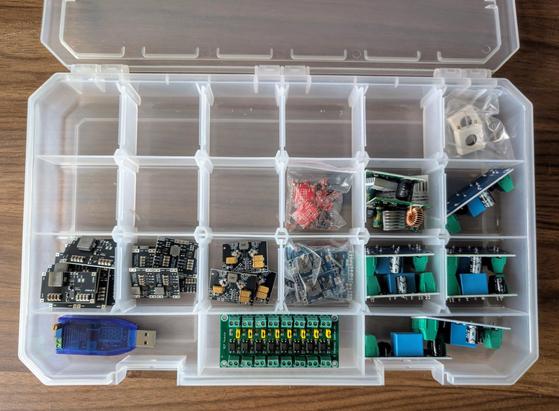 A tackle box, large clear plastic storage box with 6 by 3 dividers, for storing things. Inside are various types of modules/circuit boards that take an input voltage and output a different voltage.