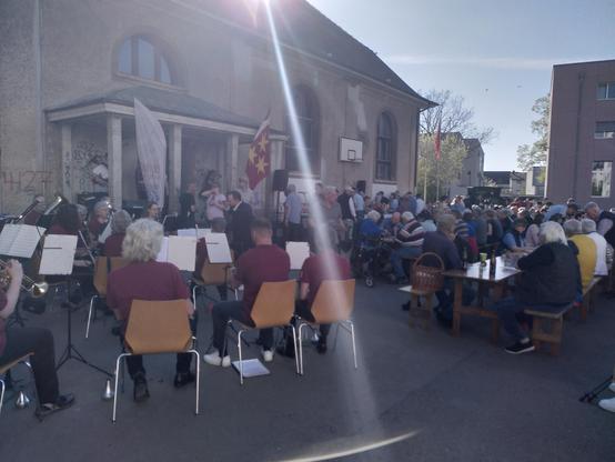 Viele Menschen an Festbänken vor der Alten Turnhalle. Im Vordergrund spielt das Musikkorps.