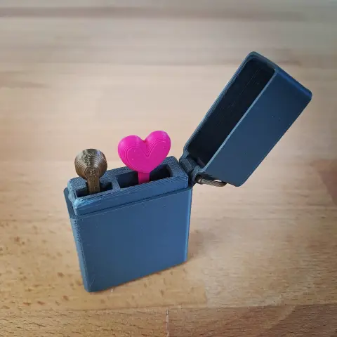 Un zippo imprimé en 3D sauf qu'au lieu de faire du feu, le mécanisme fait sortir un petit coeur.
Le zippo est gris foncé. Il est présenté ouvert et on peu y voir un bouton en PLA bronze et un cœur en PLA magenta.